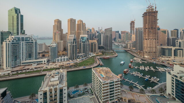 Panorama showing Dubai Marina with several boat and yachts parked in harbor and skyscrapers around canal aerial .