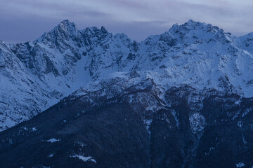 Obraz premium Sunset over the Italian alps of Valtellina, near the village of Sondrio, Italy, with fresh snow and a spectacular view of the woods and peaks - January 2023