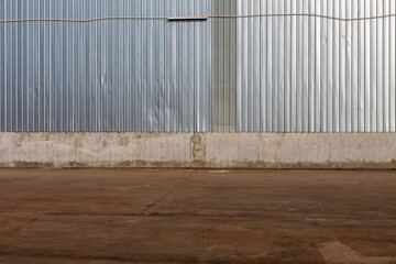 Exterior wall of warehouse made of aluminum sheet and paved road in outdoor area as background image. Texture of a wall made of silver corrugated metal sheet.