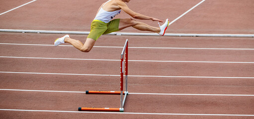 male athlete running 400 meters hurdles at stadium - obrazy, fototapety, plakaty