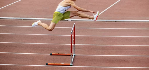 Foto op Plexiglas male athlete running 400 meters hurdles at stadium © sports photos