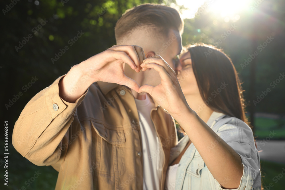 Canvas Prints Affectionate young couple kissing and making heart with hands in park