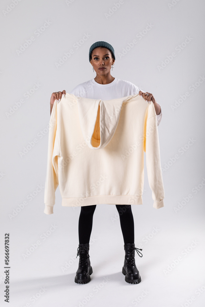 Wall mural African american woman holding a white hoodie in front of her. Mock-up.