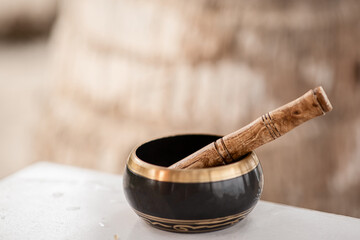 a singing Tibetan bowl stands on a table against the background of a palm tree trunk in the...
