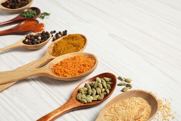 Spoons with different spices on white wooden table, closeup. Space for text