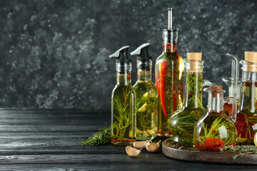 Obraz na płótnie Canvas Cooking oil with different spices and herbs in bottles on grey wooden table. Space for text