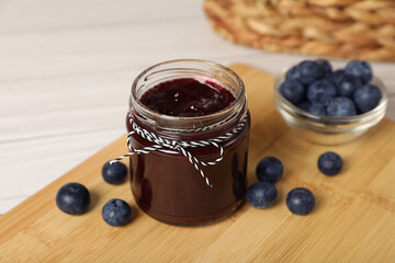 Jar of delicious blueberry jam and fresh berries on wooden table, closeup