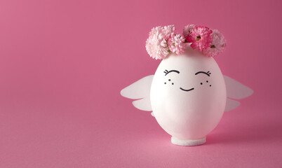 Smiling angel in a wreath of flowers. Easter egg. Pink background, space for text.