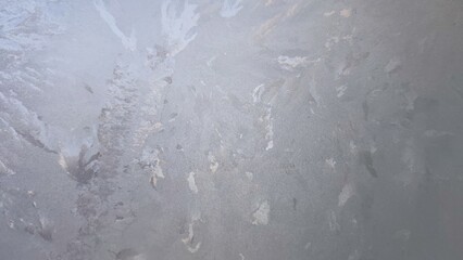 Frosty pattern on the glass window. Winter day street glass covered with a thin layer of frost. Frozen water formed a bizarre pattern on the glass, similar to the branches of a Christmas tree.