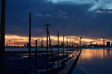 夕暮れ時の江川海岸の海上電柱と対岸に望む工場群