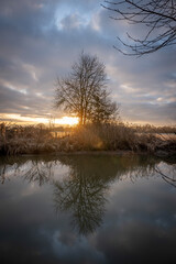 Alencon, France - 01 27 2023: Sunset in a garden near the river with trees, fields and reflection in the water