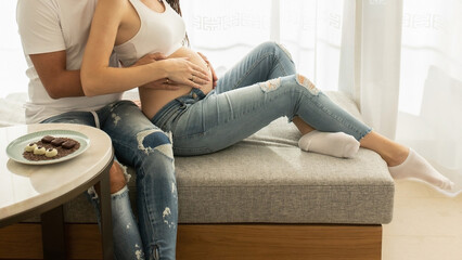 Young family expecting a baby sitting on a sofa - 566710416