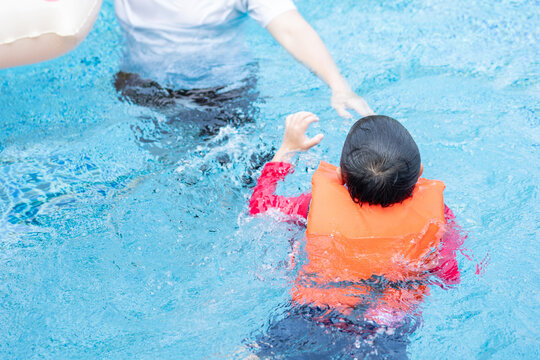 Asian boy wearing life jacket playing with father in swimming pool. Active lifestyle on summer.