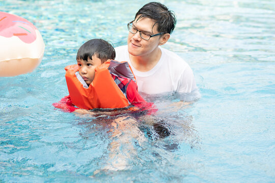 Father teaching son to swim at swimming pool. family outdoor activity on holiday in summer weather