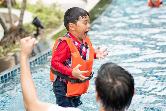 Asian boy wearing life jacket playing water in swimming pool on summer