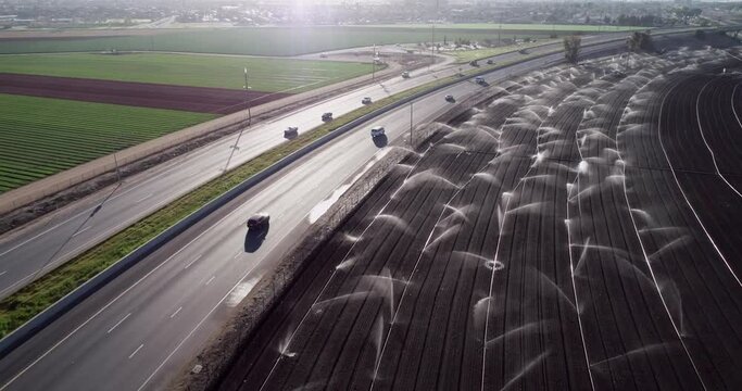 Highway and Irrigation Agriculture Field in California, United States. Sprinkler system waters rows of lettuce crops on farmland in the Salinas Valley