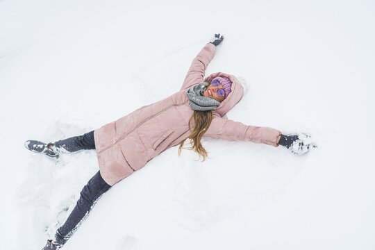 Overhead view of smiling woman lying on snow and making snow angel figure with hands and legs. High quality photo