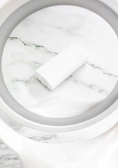 Reflection in a white round mirror of a body, face and skin care product package. Beauty products, plastics in cosmetics, sticks and daily use at home by people concerned with appearance.