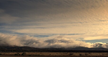 Dramatically backlit clouds and low fog flowing over the San Gabriel mountains in the Mojave region of southern California.