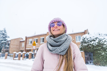 Smiling happy woman with sunglasses and winter clothes on in the snowed residential area. High quality photo