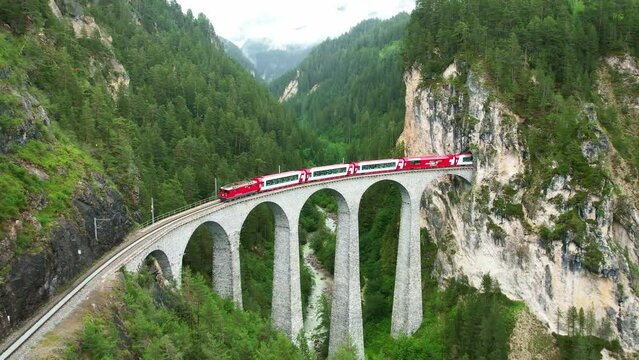 Drone Switzerland 4k. Red swiss train Glacier Express on viaduct bridge to tunnel. Landwasser, Swiss Alps. Rhaetian Railway scenic route Zermatt to St. Moritz. Switzerland summer tourism.