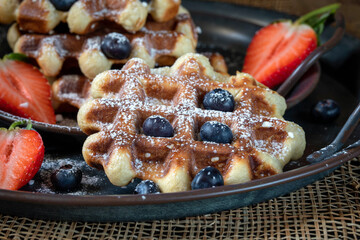 Belgian waffles decorated with strawberries, blueberries, and powdered sugar on a dark background.