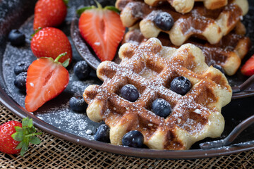 Belgian waffles decorated with strawberries, blueberries, and powdered sugar on a dark background.