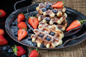 Belgian waffles decorated with strawberries, blueberries, and powdered sugar on a dark background.