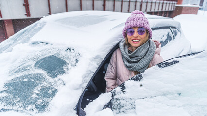 Woman in sunglasses getting into drivers seat of car under the snow in winter. High quality photo