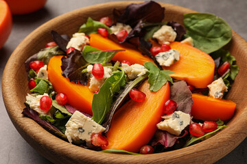 Delicious persimmon salad with cheese and pomegranate on grey table, closeup