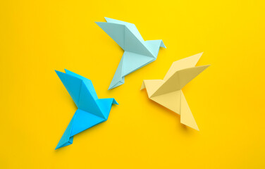 Origami art. Colorful handmade paper birds on yellow background, flat lay