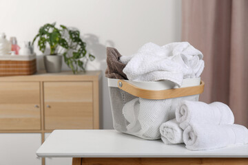 Fototapeta na wymiar Laundry basket overfilled with clothes near rolled towels on white table indoors. Space for text