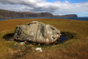 A large rock surrounded by water in front of the cliffs of Neist Point (Isle of Skye, Scotland).