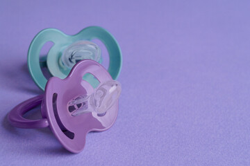 New baby pacifiers on purple background, closeup. Space for text