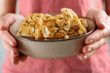 Woman holding bowl with delicious peanut kozinaki bars, closeup