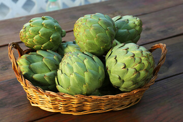 Obraz premium Wicker basket with fresh raw artichokes on wooden table