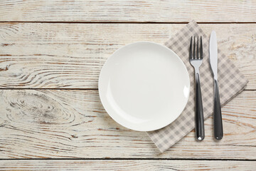 Empty plate, fork and knife on white wooden table, flat lay. Space for text