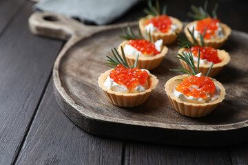 Delicious tartlets with red caviar and cream cheese served on wooden table, closeup. Space for text