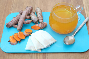 Tray with glass cup of hot tea and turmeric roots on wooden table