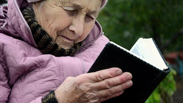 An old grandmother is reading the Bible. An elderly woman is reading the Bible. Read Holy Scripture. An old woman is reading God's Word. Pray. Christianity. Bible in old hands. Bible in wrinkled hands