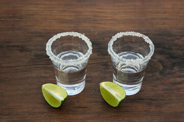Mexican tequila shots with lime slices and salt on wooden table