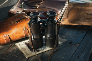 Vintage military binoculars in the leather case, laying on the wooden brown table.