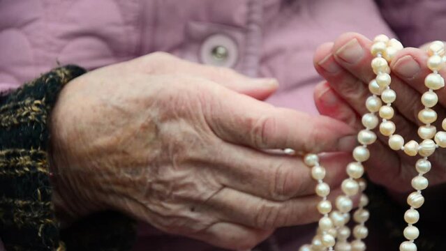 Pearls in old hands. Necklace in old hands. Wrinkled hands of an old woman. The concept of the elderly. Old hands with pearl beads. Caring for the elderly. Charity. Aged people. Jewel in old hands.