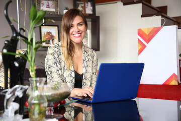 Mujer latina elegante y sonriente sentada frente a ordenador portátil, concepto de conferencia online, teletrabajo, clases virtuales, transmisión en vivo. - obrazy, fototapety, plakaty