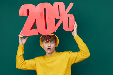 a cute, friendly man stands on a green background in bright clothes and holds a huge figure of twenty percent, his mouth wide open with emotion looks at the camera