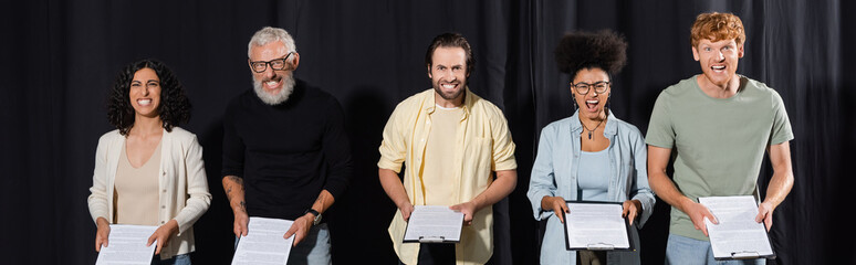 bearded art director with interracial students grimacing while holding screenplays, banner.