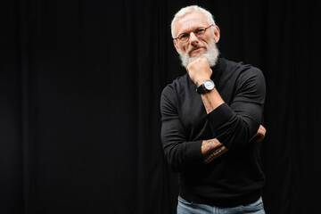 tattooed actor standing at black curtain in theater. Translation of tattoo: you have to dig deep wells if you want to get clear water.