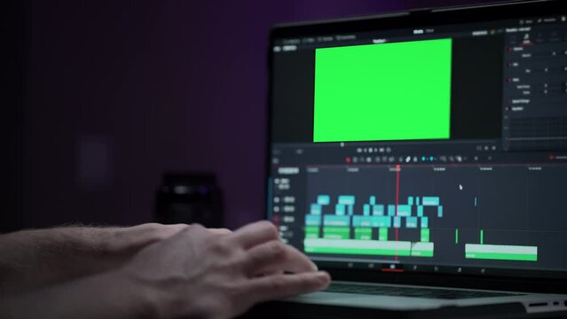 A human editor uses a laptop to creatively create a video clip. Makes color correction of video content. A freelance colorist works at home in the studio. Green screen for additional graphic picture