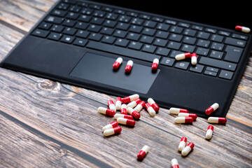 Close-up of a pile of red and white pills, on top of a wooden table next to a laptop.
