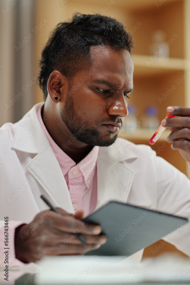 Wall mural portrait of pensive scientist checking information on tubes with blood samples and writing data in d
